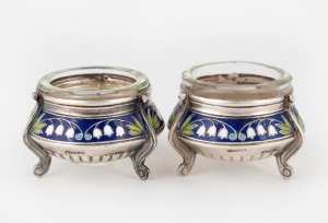 A pair of Eastern European silver salt cellars decorated with lily of the valley in enamel, with glass liners, 20th century, 3.5cm high, 5.5cm wide, 70 grams total (not including liners).