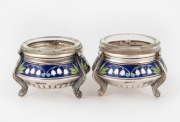 A pair of Eastern European silver salt cellars decorated with lily of the valley in enamel, with glass liners, 20th century, 3.5cm high, 5.5cm wide, 70 grams total (not including liners).