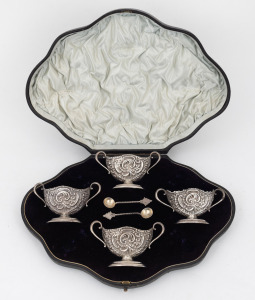 A set of four Rococo revival English sterling silver salt cellars in original plush fitted box; together with two associated spoons, 19th/20th century, made in London, circa 1894, the salts 5cm high, 10cm wide, 180 grams total.