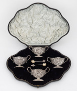 A set of four Rococo revival English sterling silver salt cellars in original plush fitted box; together with two associated spoons, 19th/20th century, made in London, circa 1894, the salts 5cm high, 10cm wide, 180 grams total.