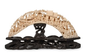 An antique Chinese carved hippopotamus tooth bridge on carved wooden stand, 19th/20th century, 16cm high, 31cm wide overall.