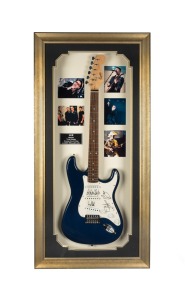 A Squier Bullet Strat electric guitar by Fender signed by all four members of U2, attractively framed with certificate of authenticity from True Blue Collectables, overall 102cm high, 59cm wide, 11cm deep