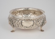 An antique English sterling silver bowl with floral repousse decoration resting on three pad feet with facemask adornments, by Charles Engelhard of London, circa 1881, 5.5cm high, 13cm wide, 166 grams.