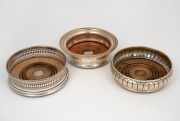 Three assorted antique and vintage sterling silver wine bottle coasters, 19th/20th century, ​​​​​​​the largest 14cm diameter, 610 grams total (including timber bases).