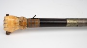 An antique poacher's walking stick with rosewood veneered shaft, finely carved whale's tooth fist grip and silver collar engraved "Load Me Well & Keep Me Clean, & When I Strike I Make A Scene" with owner's initials below "J.M.M.", 19th century, 86cm long. - 4
