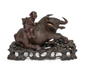An antique Chinese carved wooden buffalo with rider figural group, adorned with glass eyes and carved bone teeth, displayed on original carved timber stand, Qing Dynasty, 19th century, 20cm high, 33cm wide