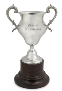 RMS LUSITANIA (CUNARD LINER) antique sterling silver presentation trophy cup, engraved "Floreat Lusitania" on original turned timber plinth. Made by Daniel George Collins of Sheffield, circa 1910. The cup 26.5cm high, 37cm high with base, 700 grams. Accompanied by a postcard of the ill-fated Lusitania, which was sunk by German U-boats in 1915, resulting in the deaths of 1,197 people including many prominent Americans.