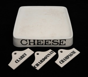 A vintage porcelain cheese stand; together with three porcelain wine cellar labels (Claret, Chardonnay and Champagne), 20th century, (4 items), the stand 6.5cm high, 33cm wide, 33cm deep.