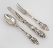 A three piece sterling silver christening cutlery set comprising of a knife, fork and spoon, all attractively decorated with putti figures, made in Sheffield, circa 1875, the knife 19.5cm long, 128 grams including filled knife handle.