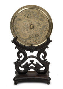 An ornamental Chinese bronze mirror with engraved dragon decoration on carved rosewood stand, 19th/20th century, ​​​​​​​61cm high overall.
