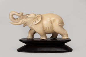 A carved ivory elephant statue on carved timber base, early to mid 20th century, 7cm high overall including base, 10cm long.