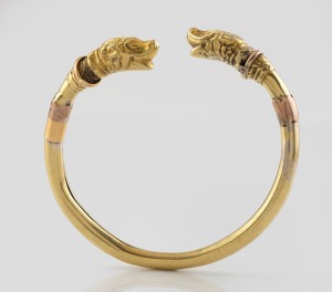 An antique 18ct gold bangle in the Celtic revival style decorated with heads of mythical creatures, 19th century, note: missing safety chain, possibly wax filled, 18.7 grams total.