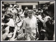 DON BRADMAN - DECEMBER 1948 MCG TESTIMONIAL MATCH: Original press photograph showing Bradman leading his team onto the Melbourne Cricket Ground through a throng of supporters; 15 x 20cm.
