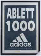 Various framed items including the Herald Sun banner "ABLETT BOWS OUT", a full-page poster of Polly Farmer, an "ABLETT 1000 ADIDAS" poster, an Essendon 1997 team photo, and a photo of Tim Watson in his Essendon jumper; the largest 72 x 52.5cm. (5 items) - 3