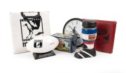 CLUB-BRANDED ITEMS: Group of six items, comprising Magpies clock, cushion, and Angove's Tawny Port decanter, Essendon cushion and 1993 Premiers metal trading cards tin, and Fitzroy boot-shaped decanter. (6 items)