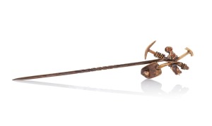 An antique 15ct gold miner's stickpin with crossed pick and shovel, housed in a plush fitted box, 19th century, 7.5cm high, 2.5 grams.