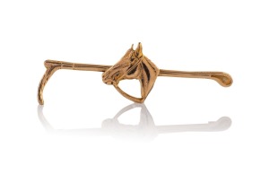 An antique 9ct gold jockey's brooch with riding crop and horse's head, housed in a plush fitted box branded "NEWMAN'S New Address, 289, Collins St. E. 1 Door From Elizabeth St.", 5.2cm wide, 2.9 grams.