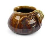 REMUED brown and green glazed pottery jug with applied juvenile gum leaves and gumnuts with branch handle, incised "Remued", ​​​​​​​11cm high, 16cm wide.