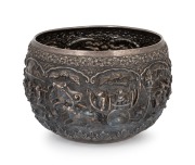An impressive antique Burmese silver bowl adorned with repousse vignettes and inscribed with a dedication dated 1902, ​​​​​​​20cm high, 28cm wide, 1800 grams.