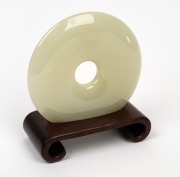 A Chinese carved jade bi disc on timber stand, 19th/20th century, ​​​​​​​15.5cm diameter.