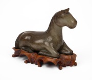 A Chinese carved jade horse statue on wooden stand, 20th century, ​​​​​​​13cm high, 15cm long overall.