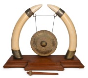An impressive dinner gong, crafted from ivory tusks mounted in gilt metal, resting on a teak base, early to mid 20th century, an imposing 70cm high, 93cm wide, 31cm deep.