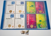 1956 MELBOURNE OLYMPICS: Seat cushion from the opening ceremony, chocolate tin, boomerang ornament and badge; together with SYDNEY 2000 badges and medallions, (qty). - 5