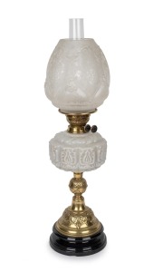 An antique oil lamp with milk glass font, black button burner, acid etched shade and glass chimney, mounted on an ornate black ceramic and brass base, 19th/20th century, 65cm high.