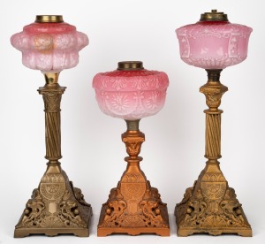 Three assorted oil lamps with pink glass fonts and cast metal bases, (parts only), the largest 48cm high.