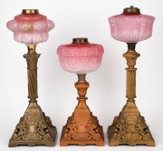 Three assorted oil lamps with pink glass fonts and cast metal bases, (parts only), the largest 48cm high.