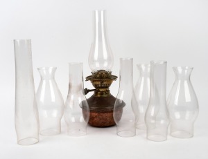 An antique copper and brass oil lamp with black button double burner and eight assorted glass chimneys, 19th/20th century.
