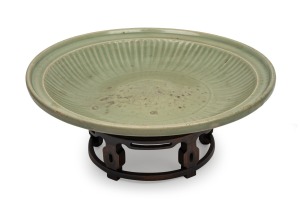 An impressive antique Chinese celadon glazed charger, Yuan/Ming Dynasty, displayed on an antique huanghuali stand, 44.5cm diameter.