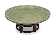 An impressive antique Chinese celadon glazed charger, Yuan/Ming Dynasty, displayed on an antique huanghuali stand, 44.5cm diameter.