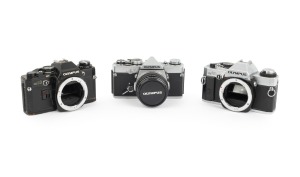 OLYMPUS: Group of 1970s SLRs, comprising Olympus OM-1 (F. Zuiko Auto-S 50mm f1.8, with cap and leather case), Olympus OM10 (body only), and Olympus OM20 (body only). (3 items)