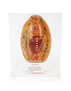 An artwork titled "Football Spirits" by Australian indigenous artist Kathleen Kemarre Wallace (1948 - 2024), comprising a football decorated with an intricate design in yellow, black, white, and gold; housed in bespoke perspex case measuring approx. 30 x 24 x 24cm.