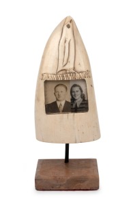 An unusual scrimshaw whale's tooth with carved penguin decoration and inset black and white photo portraits, mounted on later bespoke stand, circa 1930s, the tooth 15.5cm high.