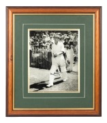 DON BRADMAN: Framed and glazed photograph print of Bradman stepping out to bat at the MCG, featuring Bradman's original signature in permanent marker; 45 x 39cm overall.
