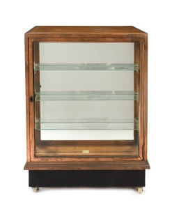 An antique Tasmanian oak and copper bound shop display cabinet with four large drawers and unusual slimline display case front, circa 1900, electrified and on later casters, 104cm high, 77cm wide, 62cm deep.