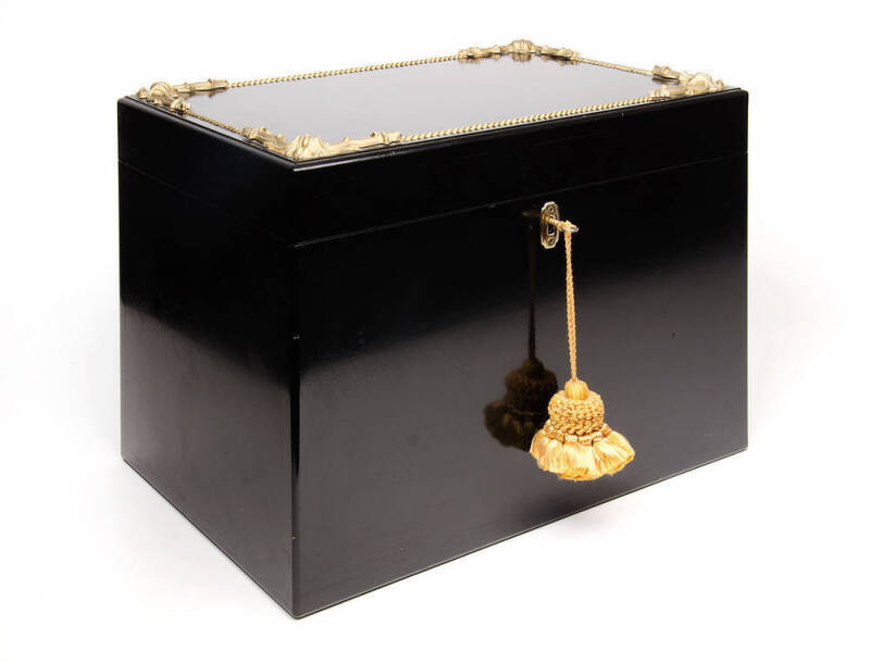 Ebonised wood piano music box with applied gilt gesso to the lid, brass escutcheon with gold silk tassel.