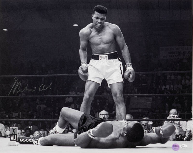 MUHAMMAD ALI, signed b/w photograph of Ali standing over Sonny Liston, size 51x41cm. With 'Online Authentics' No.OA-8090305.